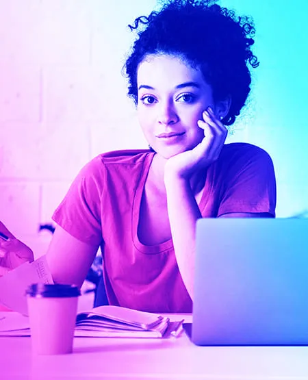 Femme souriante assise à un bureau avec un ordinateur portable, un carnet et un café
